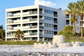 A multi-story hotel with balconies, a sandy foreground, and palm trees. - Siesta Sands - Unit 611 (Siesta Key)