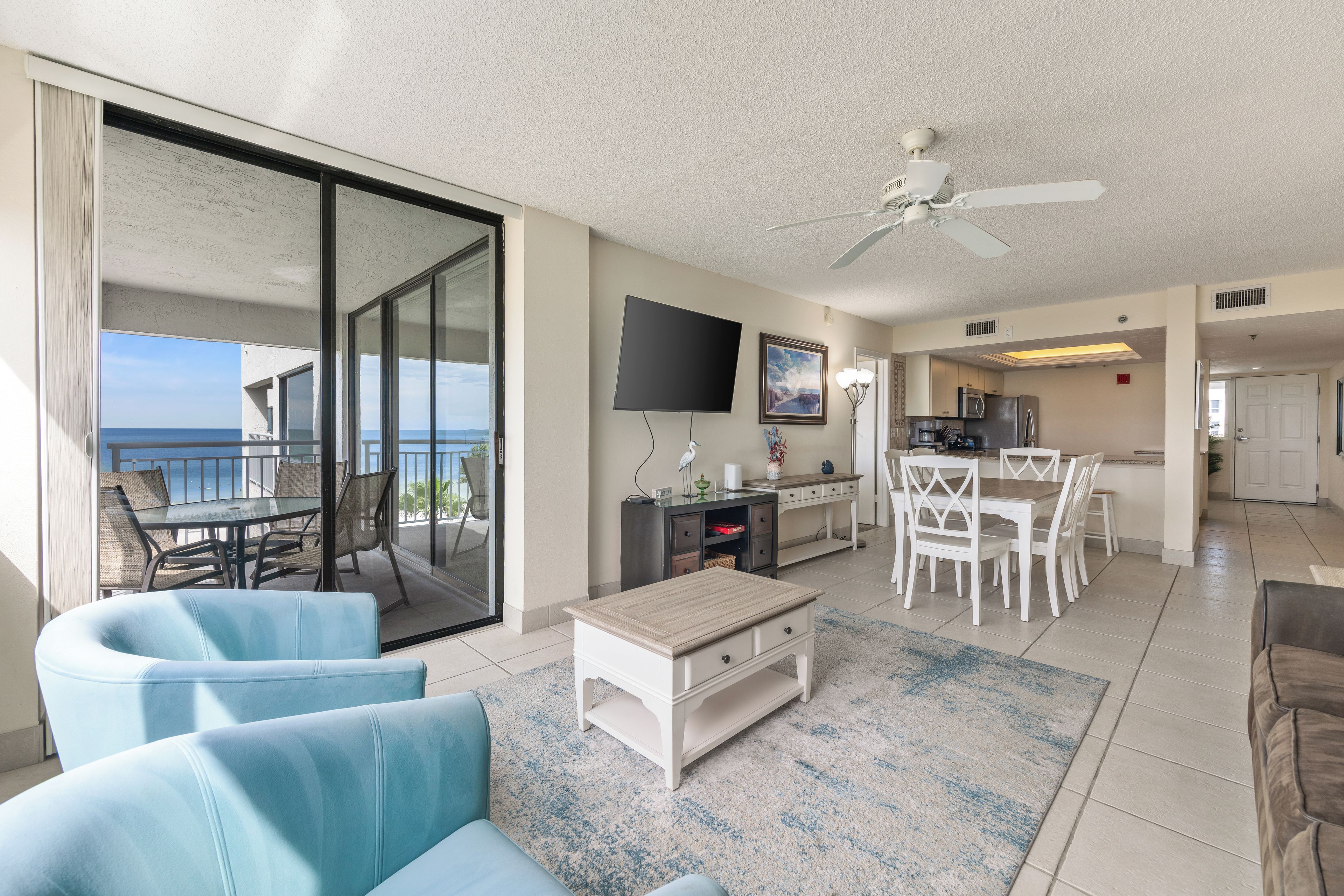 A hotel room with a balcony, a dining area, a kitchen, and a flat-screen TV.