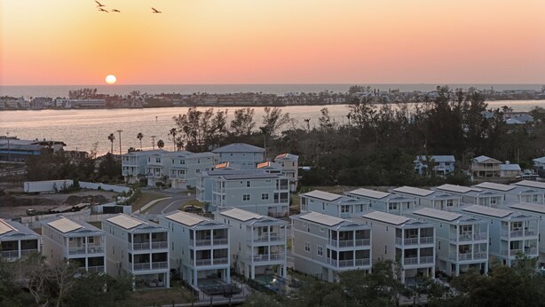 Uma área residencial costeira com edifícios altos, piscina visível e um pôr do sol sobre a água.