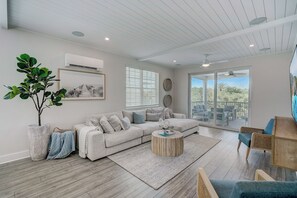 A modern living room with a sectional sofa, a coffee table, and a large window with blinds. - Hunters Point Resort and Marina Mainsail (Cortez)