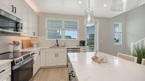 A modern kitchen with white cabinetry, stainless steel appliances, and a large island. - Hunters Point Resort and Marina Mainsail (Cortez)