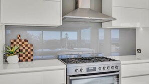 A modern kitchen with a stainless steel stove, a checkered cutting board, and a potted plant. - Belle Mer - Bega Street 4 Tathra (Tathra)