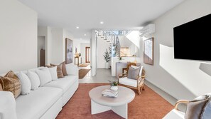 A modern living room with a white sofa, a round coffee table, and a staircase leading to an upper level. - Belle Mer - Bega Street 4 Tathra (Tathra)