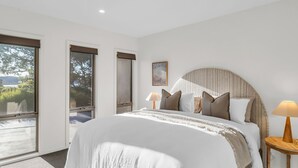 Ein Schlafzimmer mit einem großen Bett, einem hölzernen Kopfteil und Blick ins Freie durch eine Schiebetür.