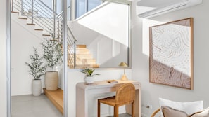 Ein modernes Interieur mit einer Treppe, einem Schreibtisch mit Stuhl, einem großen gerahmten Kunstwerk und Topfpflanzen.