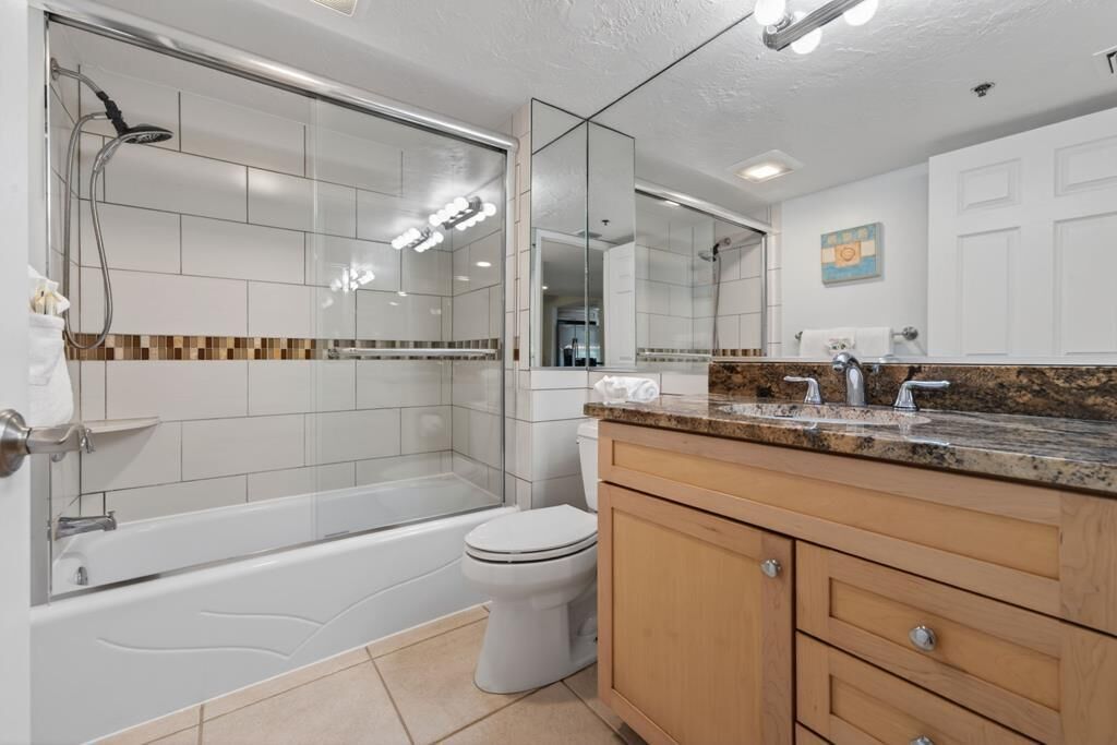 Un baño moderno con ducha envuelta en vidrio, inodoro blanco y tocador de encimera de granito.