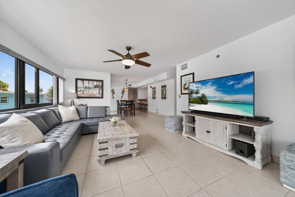 A modern living room with a grey sofa, a wooden coffee table, a flat-screen TV, and a ceiling fan.