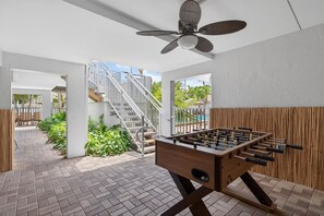 An indoor space with a foosball table, a ceiling fan, and a staircase leading to an outdoor area with plants and a pool. - Siesta Sands - Unit  208 (Siesta Key)