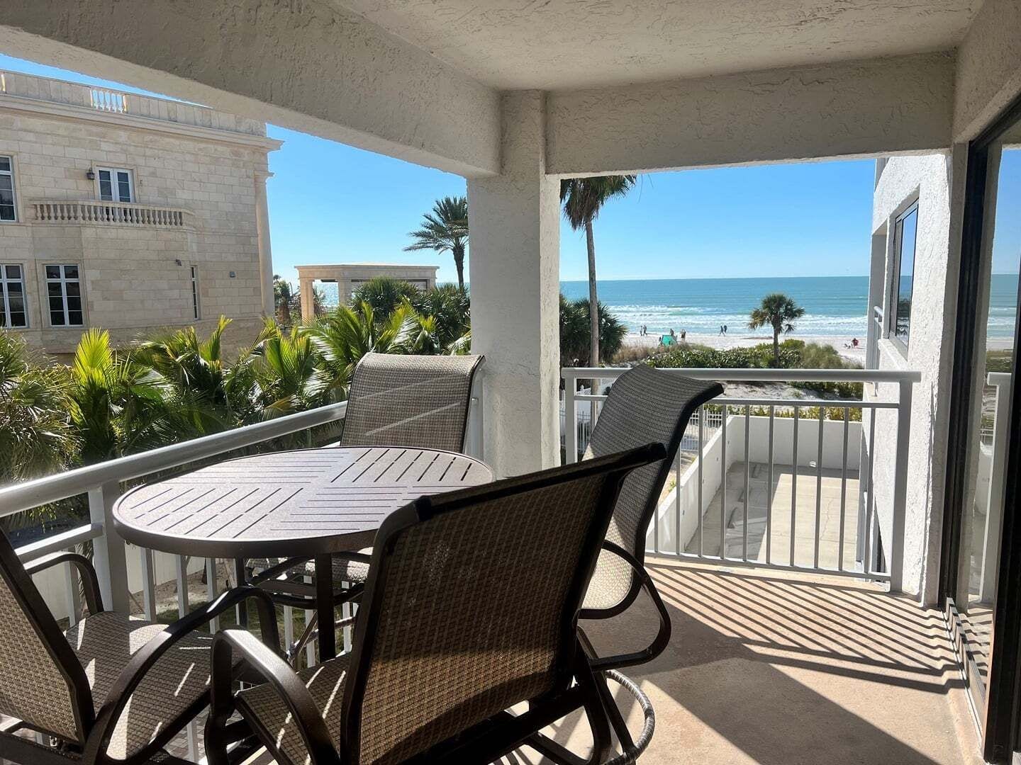 A balcony with a table and chairs, overlooking a beach and ocean.
