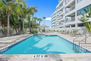 A swimming pool with a 4 ft 6 in depth sign, surrounded by palm trees and a building with balconies. - Siesta Sands Unit 309 (Siesta Key)