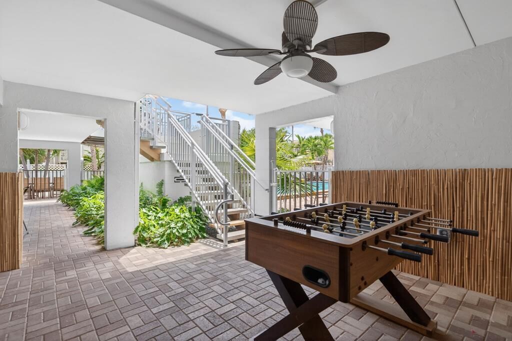 An indoor space with a foosball table, a ceiling fan, and a staircase leading to an outdoor area with plants and a pool.