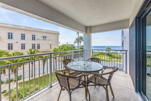 A balcony with a glass table and wicker chairs, overlooking a street with palm trees and a building. - Siesta Sands - Unit 310 (Siesta Key)
