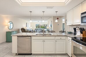 A modern kitchen with white cabinetry, a built-in dishwasher, a stainless steel oven, and a granite countertop. - Siesta Sands - Unit 310 (Siesta Key)