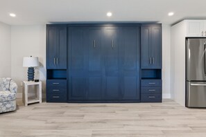 A room with a large dark blue wardrobe, a patterned sofa, a small table with a lamp, and a stainless steel refrigerator. - Pool-view 1BR condo in Siesta Key with kitchen, WiFi, and heated pool. (Siesta Key)