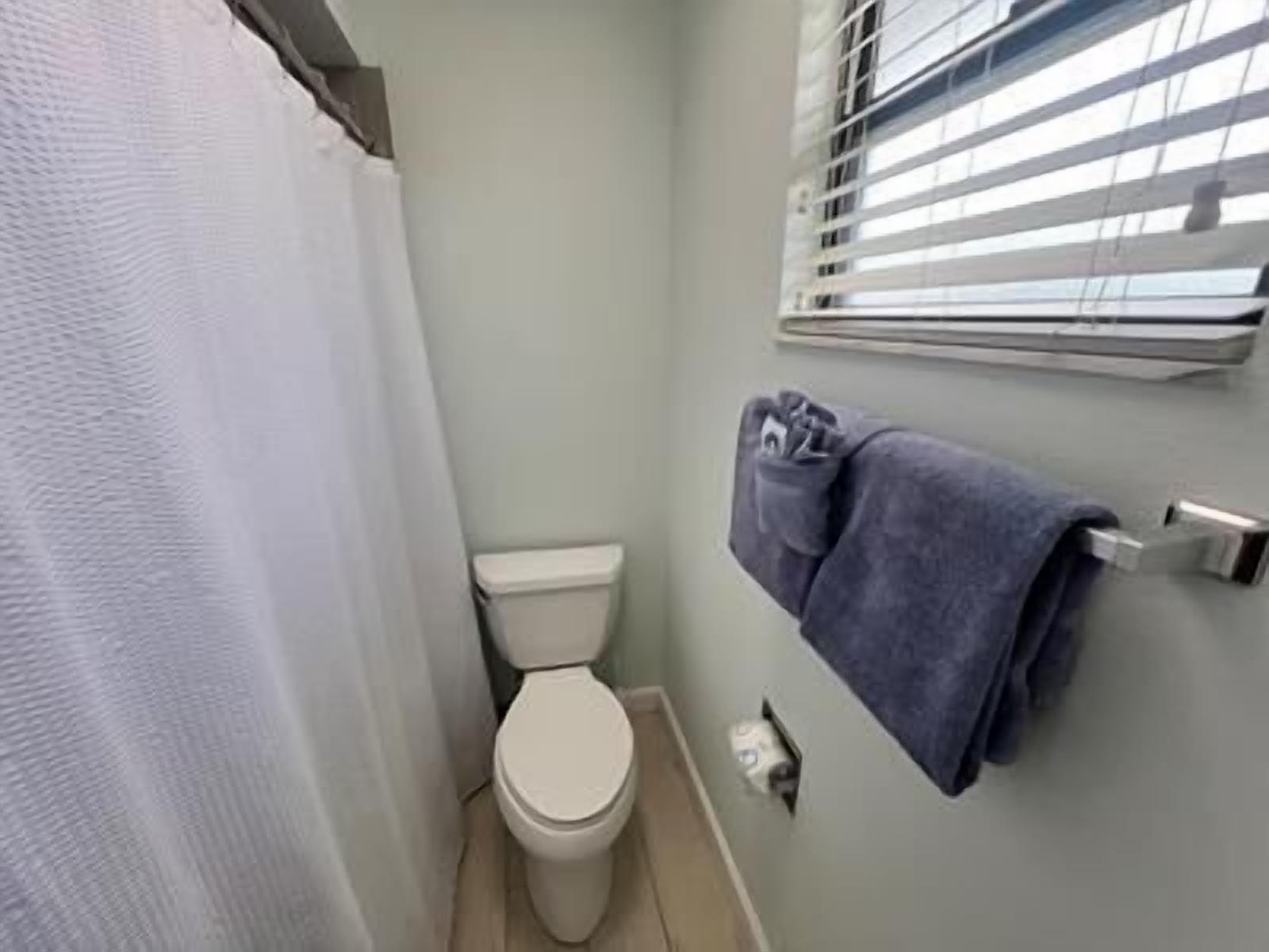 Et lille badeværelse med toilet, et håndklædestativ med håndklæde og et vindue med persienner.