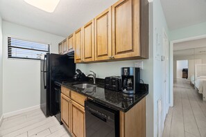 A compact kitchen with wooden cabinets, a black refrigerator, a dishwasher, a coffee maker, and a toaster. - Siesta Sands Unit 204 (Siesta Key)