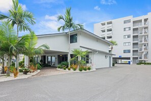A modern building with a covered entrance, palm trees, and a parking area. - Siesta Sands Unit 204 (Siesta Key)