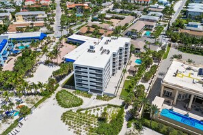 A multi-story hotel with a rooftop pool, surrounded by palm trees and a sandy beach area. - Siesta Sands Unit 204 (Siesta Key)