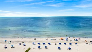 A beach with clear blue water, people swimming, and numerous beach umbrellas and chairs. - Siesta Sands Unit 204 (Siesta Key)