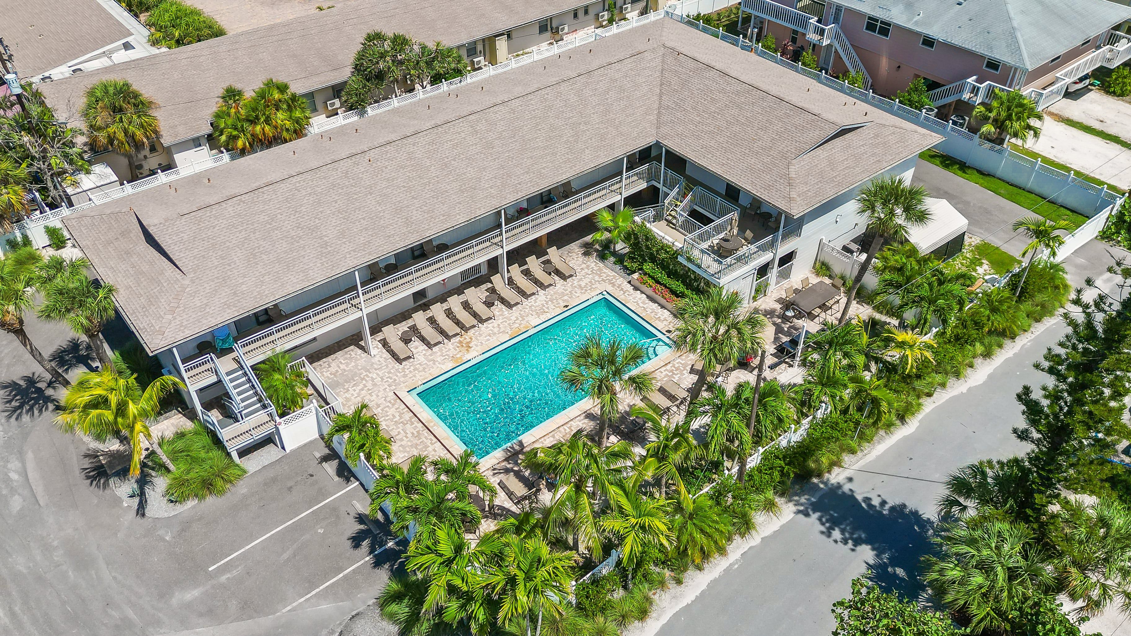 Vista aérea de um hotel com piscina, cercado por palmeiras e espreguiçadeiras.