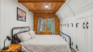 Una camera da letto con soffitto in legno, un letto con biancheria da fiori, un comodino, una lampada, una finestra con tende e un armadio a parete.