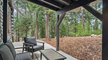 A covered outdoor seating area with a sofa and a table, overlooking a forested area.
