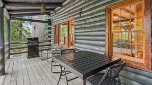 Une cabane en rondins dotée d’un patio couvert, d’un barbecue et d’une table avec des chaises.