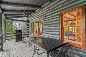Una cabaña de troncos con un porche cubierto, una parrilla y una mesa con sillas.