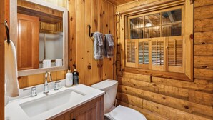 Une salle de bain rustique, avec des murs en bois, comprenant un lavabo, un miroir et une fenêtre.
