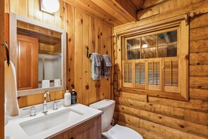 Baño de cabaña de madera con lavabo, espejo y ventana.