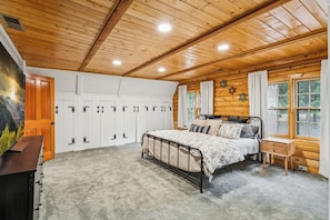 Un dormitorio con techo de madera, cama con estructura metálica, mesita de noche y ventana con cortinas.