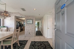 A modern kitchen with a dining area, a hallway leading to a door, and a blue house number sign. - Siesta Sands - Unit 508 (Siesta Key)