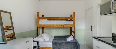 Una cama litera con escritorio y silla, un espejo y un microondas en una habitación pequeña con armarios blancos y piso de baldosas.