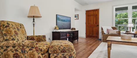 Un salon comprenant un canapé, une table basse, une lampe, un téléviseur et une porte en bois.