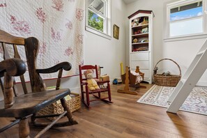 Une pièce chaleureuse avec un fauteuil à bascule, une petite chaise rouge, une bibliothèque et un panier en osier posé sur le sol.