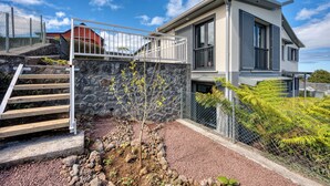A modern two-story house with a stone retaining wall, a metal fence, and a staircase leading to the upper level. - Ti Kaz Komela - Vue montagnes - Terrasse (Le Tampon)
