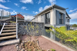 A modern two-story house with a stone retaining wall, a metal fence, and a staircase leading to the upper level. - Ti Kaz Komela - Vue montagnes - Terrasse (Le Tampon)
