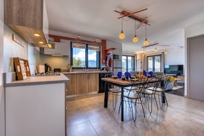 A modern kitchen with a dining area, large windows, and a TV in the living room. - Ti Kaz Komela - Vue montagnes - Terrasse (Le Tampon)
