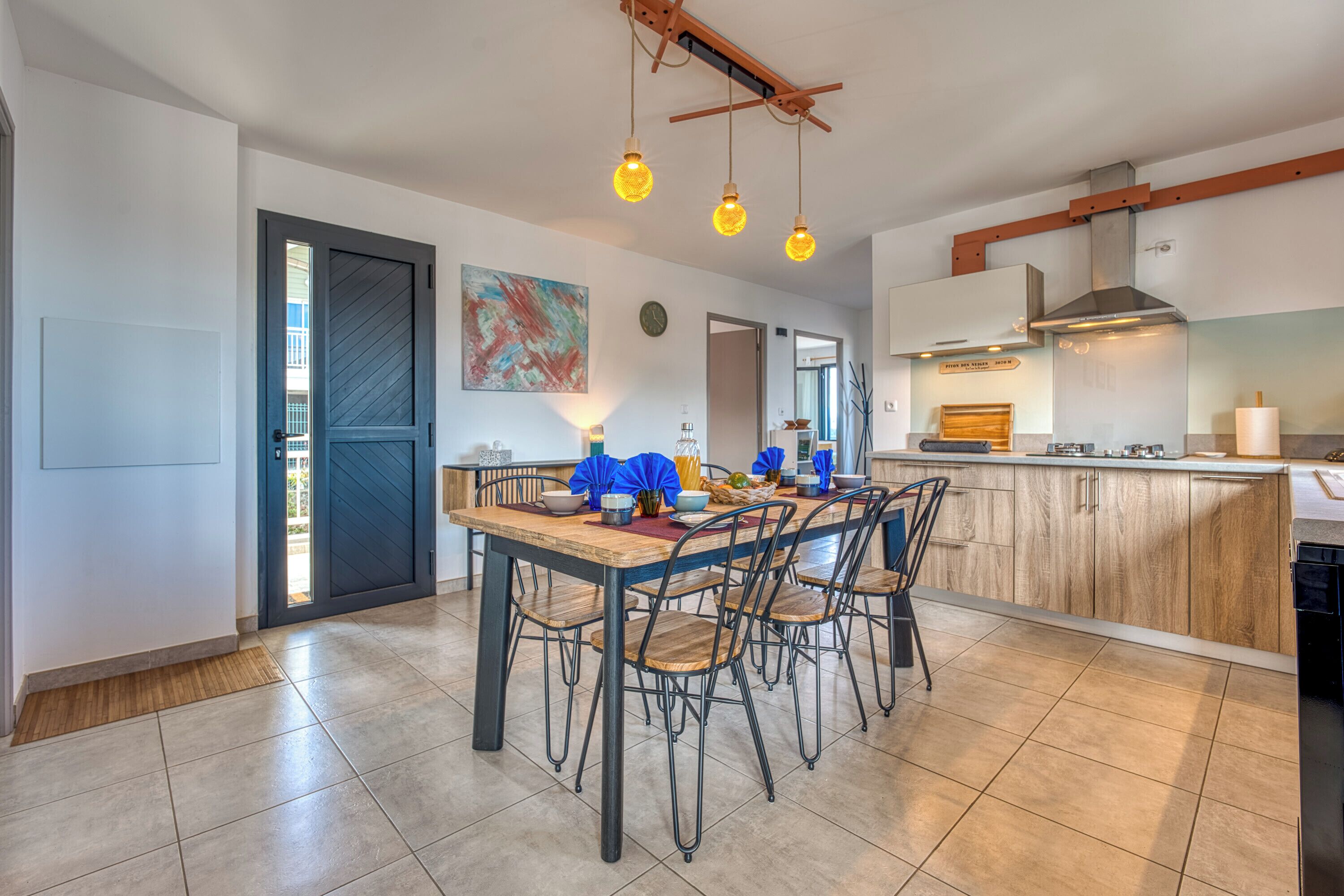 A modern kitchen with a dining area, featuring a wooden table, chairs, and pendant lighting.