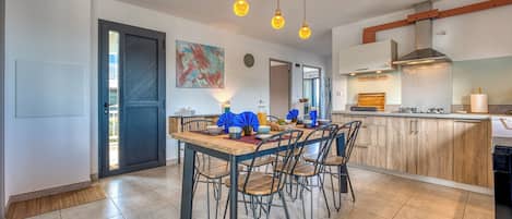 Une cuisine moderne avec un coin repas, comprenant une table en bois, des chaises et des luminaires suspendus.