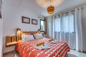 Ein Hotelzimmer mit Bett, Holz-Kopfteil, zwei Wandlampen, einem Fenster mit Vorhängen und einem Kunstwerk an der Wand.