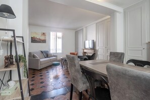 A modern living room with a sofa, a dining table with chairs, a TV, and a painting on the wall. - La Charmante - Centre-ville - Wifi (Le Mans)