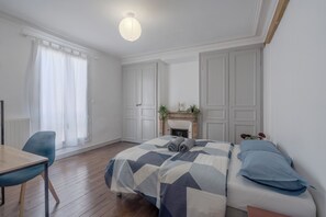 A bedroom with a bed, a chair, a fireplace, and a window with curtains. - La Charmante - Centre-ville - Wifi (Le Mans)
