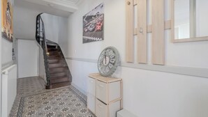 Um corredor com piso estampado, escada de madeira, relógio de parede e quadro emoldurado.