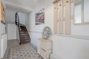 A hallway with a patterned floor, a wooden staircase, a wall clock, and a framed picture. - La Charmante - Centre-ville - Wifi (Le Mans)