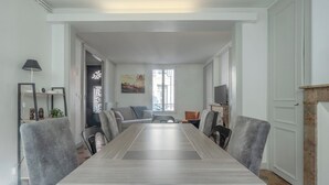 Uma sala de jantar com uma mesa comprida, cadeiras, um sofá e uma televisão.