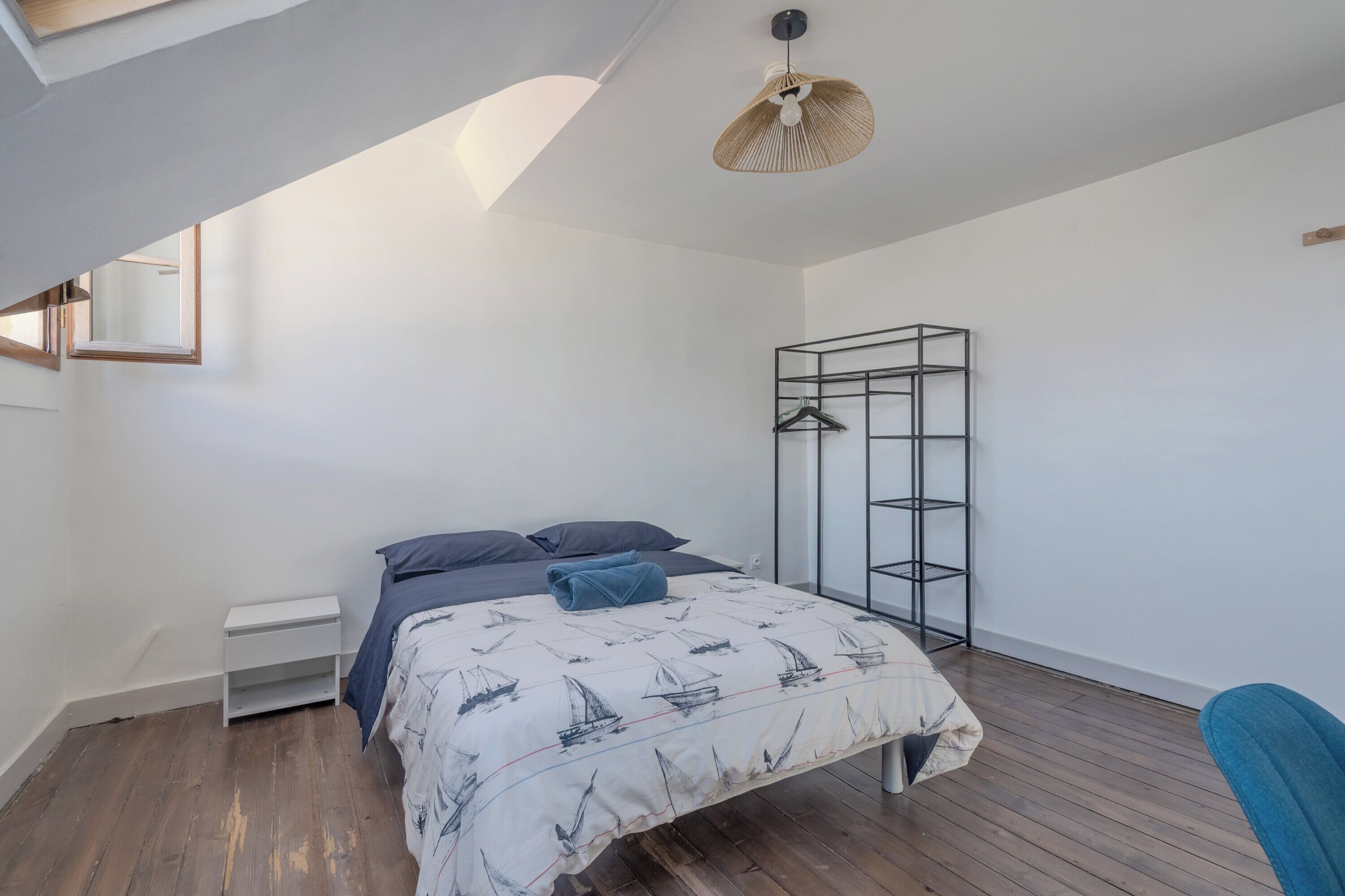 A bedroom with a bed, a wardrobe, a hanging light fixture, and a window.
