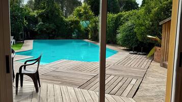 Vista a través de un ventanal de madera que da a una piscina, rodeada de follaje.