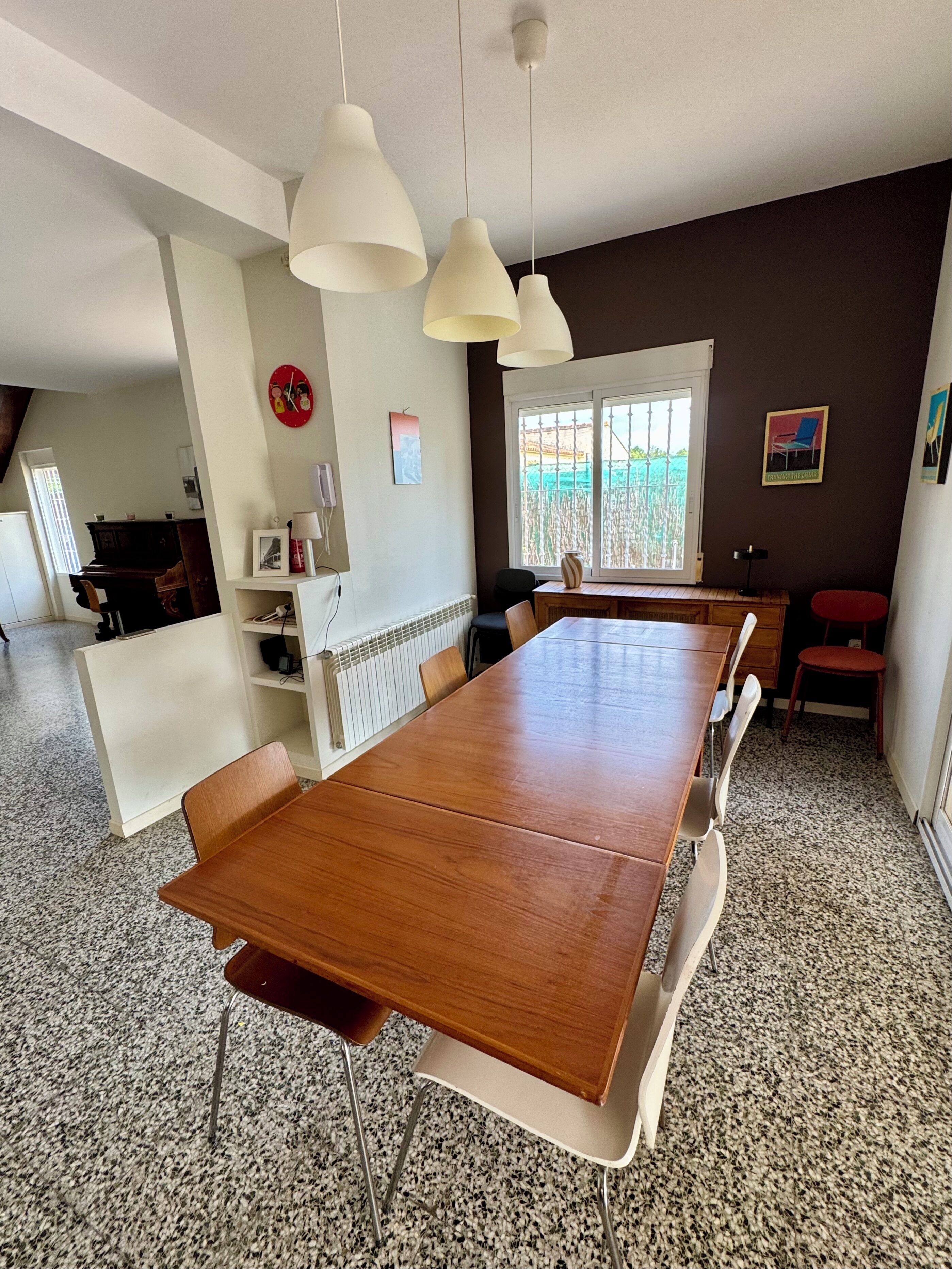 Un comedor con una larga mesa de madera, sillas blancas y lámparas colgantes.