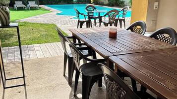 Un patio exterior con mesa y sillas de madera, una piscina y un jardín.
